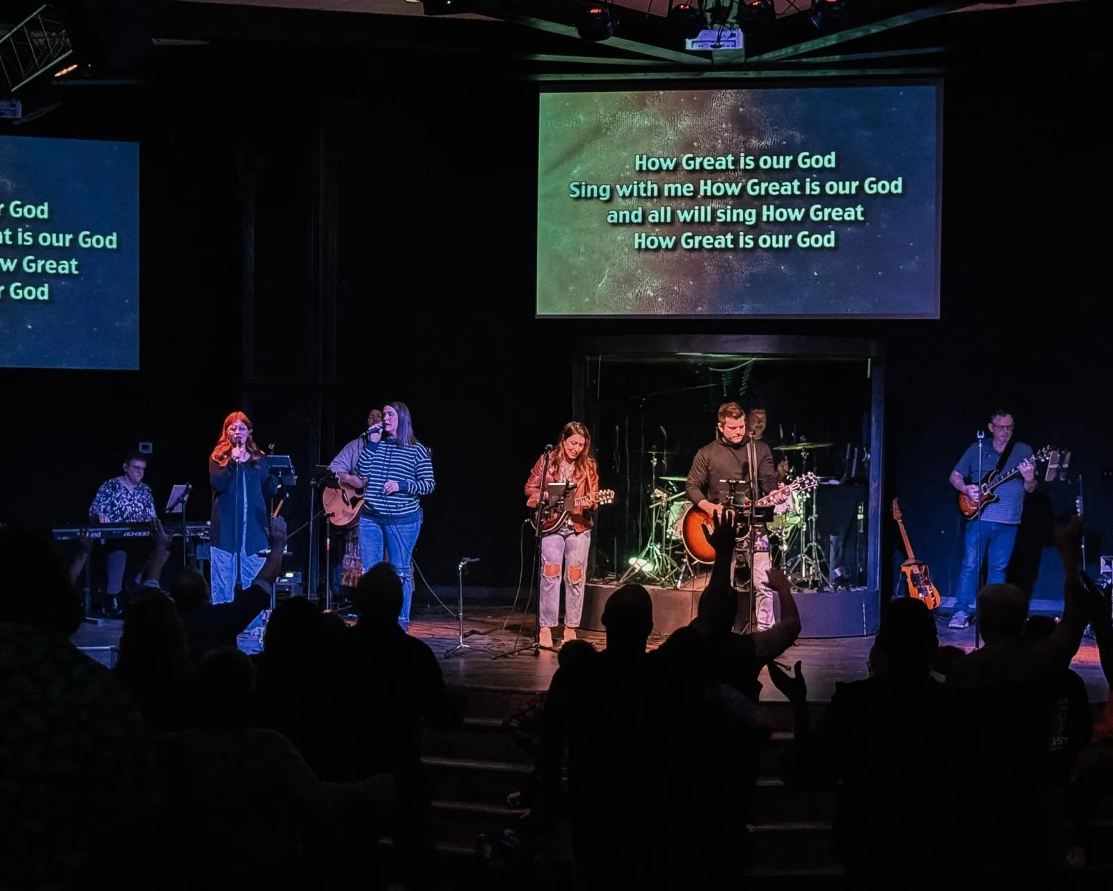 The IFC worship team leading a song on stage while the congregation stands with hands raised